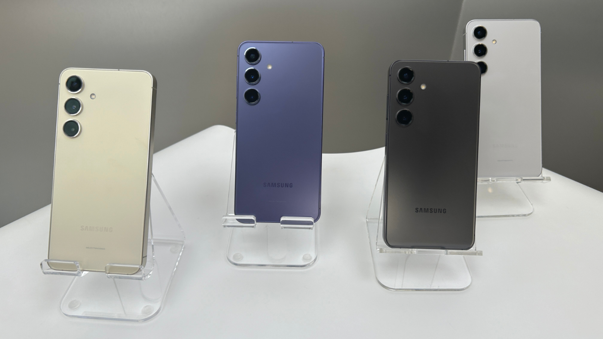 four different colors of the samsung galaxy s24 lined up in clear stands on a white surface