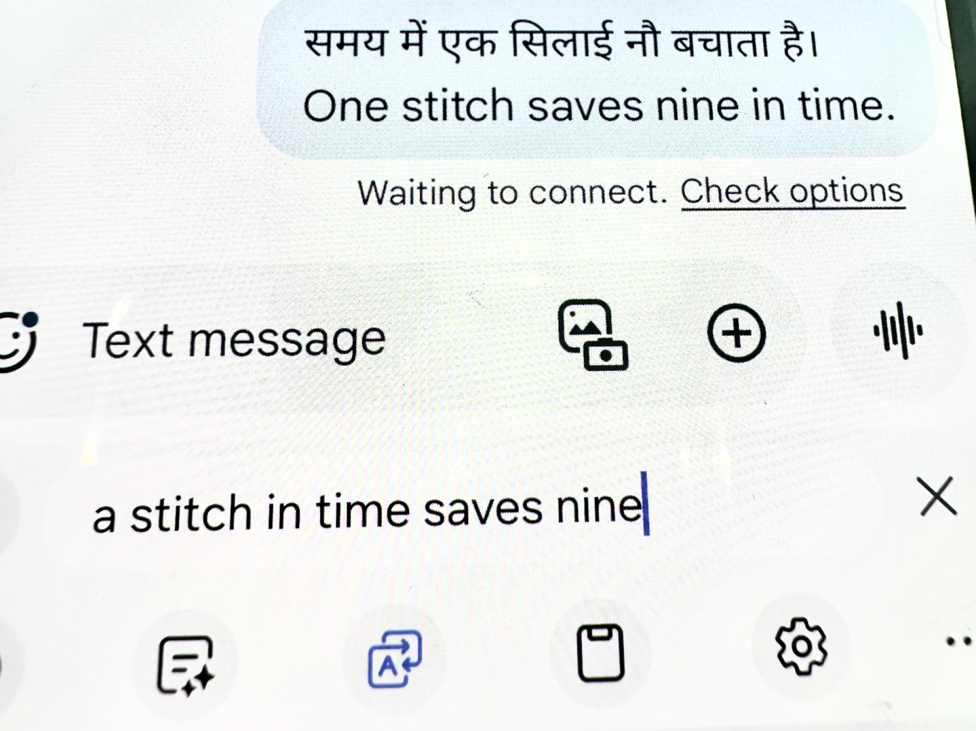 The phrase "a stitch in time saves nine" is translated into Hindi on a phone screen.